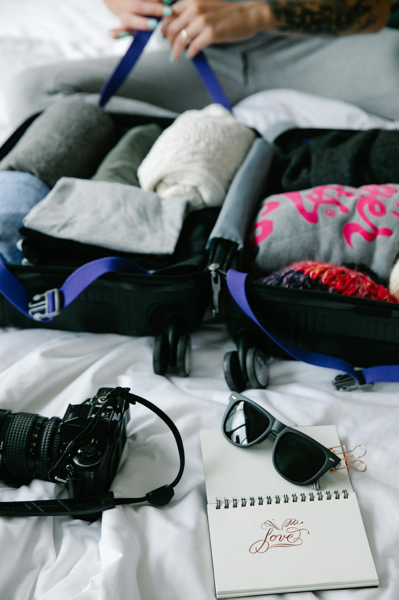 A person packs their suitcase with clothes and travel essentials on a bed.